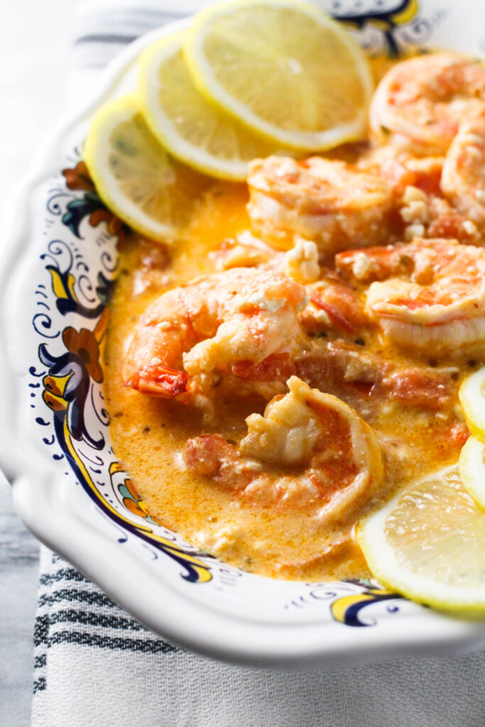 Shrimp with feta and tomatoes in a bowl garnished with lemon slices.