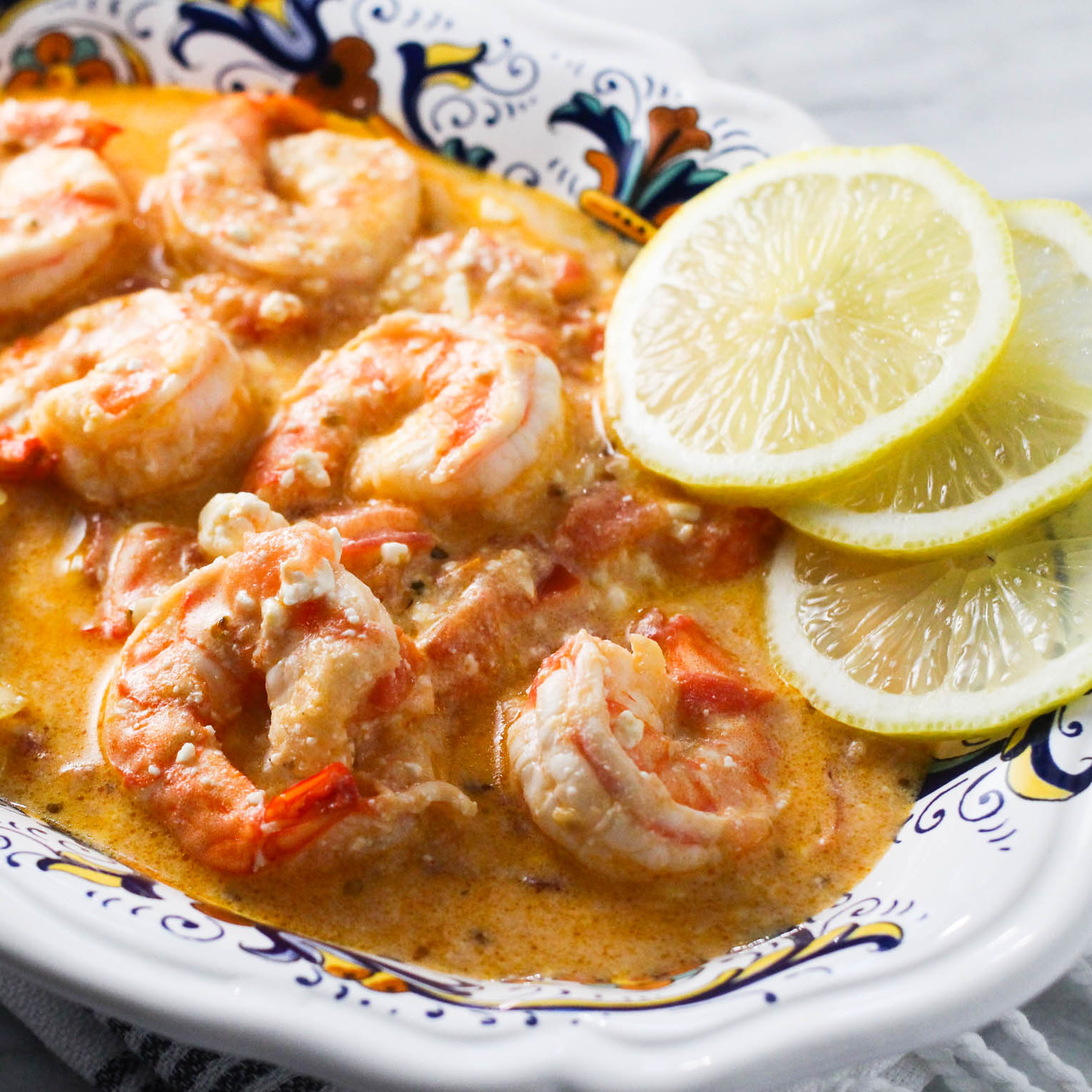 Shrimp with feta and tomatoes in a bowl garnished with lemon slices.