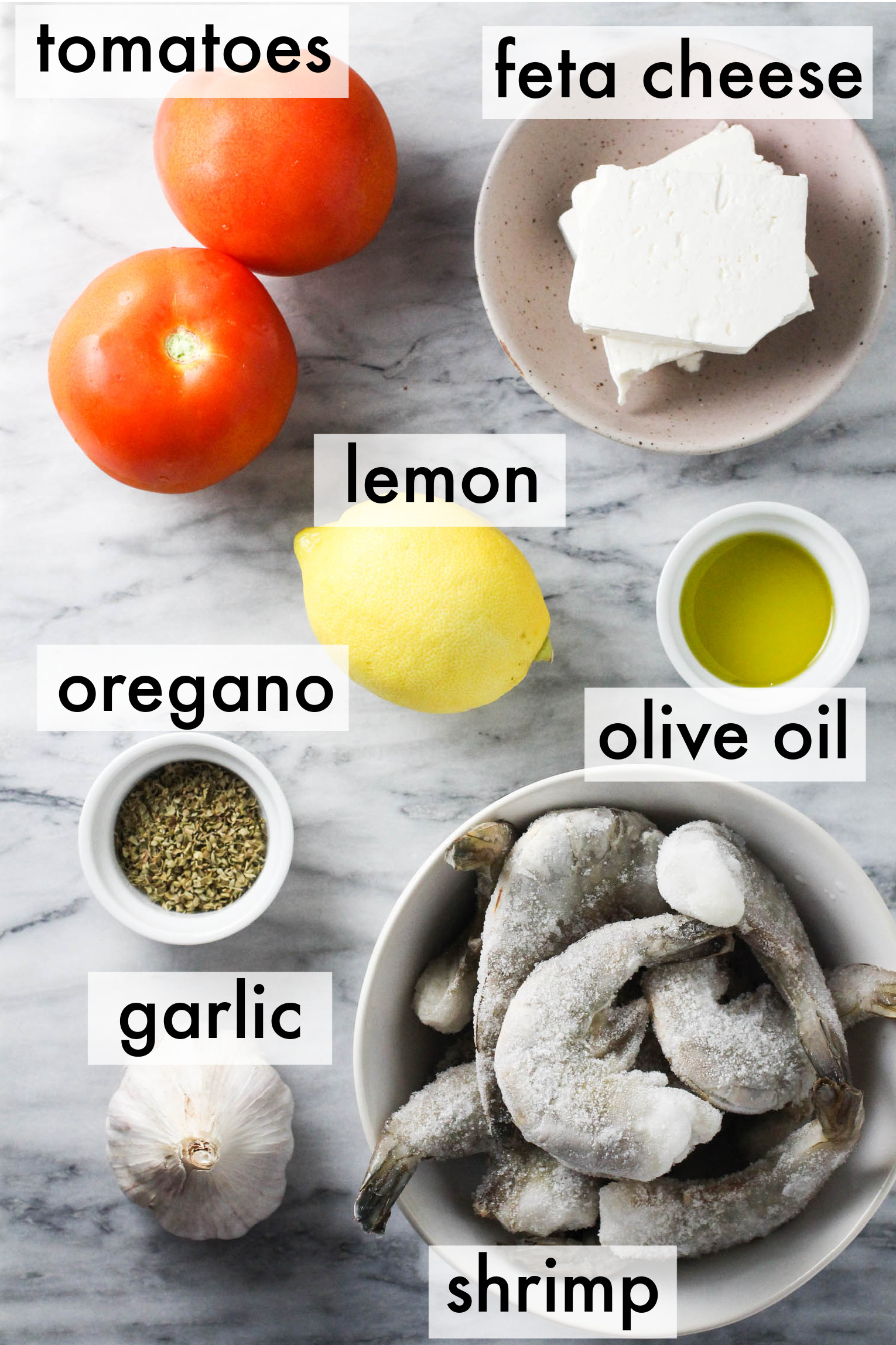 Recipe ingredients displayed on a marble background. The ingredients are labeled as follows: tomatoes, feta, lemon, oregano, olive oil, garlic, shrimp.