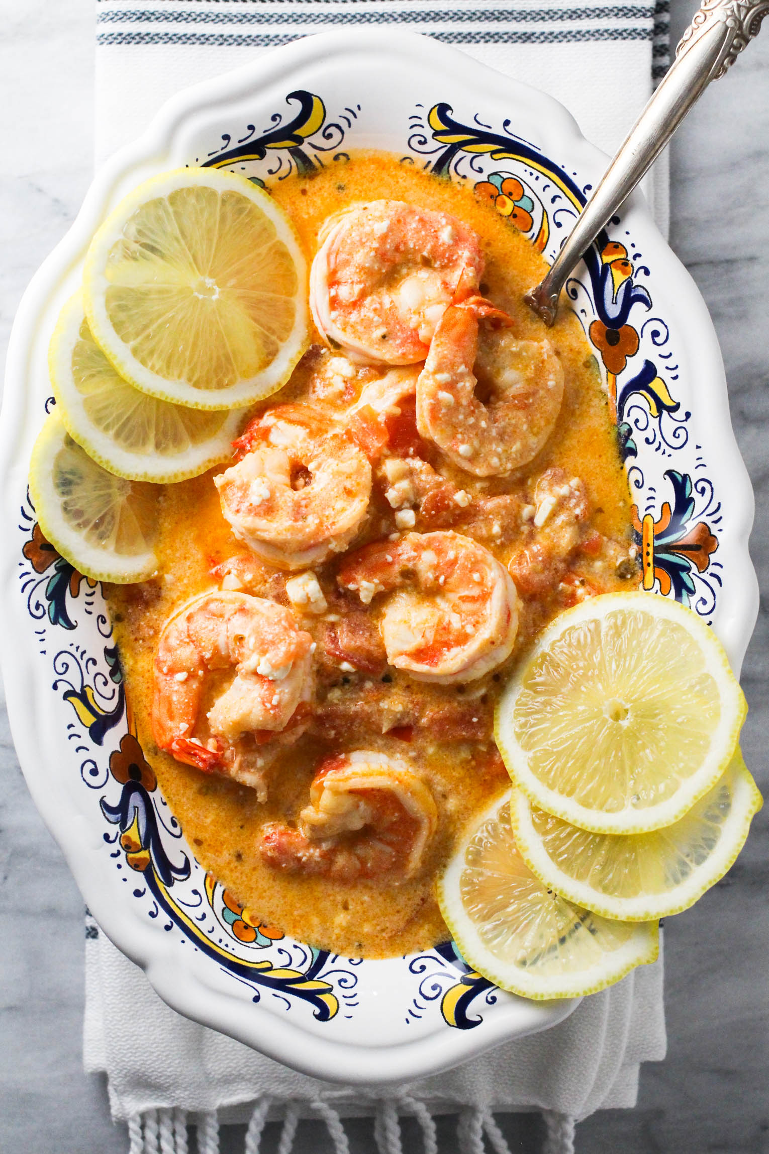 Overhead shot of shrimp with feta and tomatoes in a bowl garnished with lemon slices.