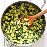 Sauteed zucchini in a pot with a wooden spatula.