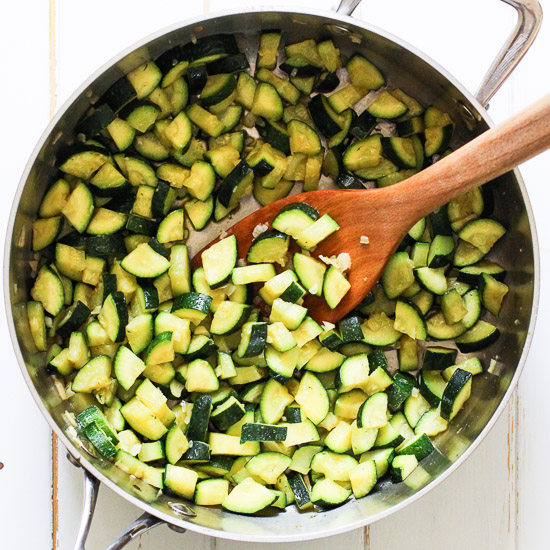 Sauteed zucchini in a pot with a wooden spatula.