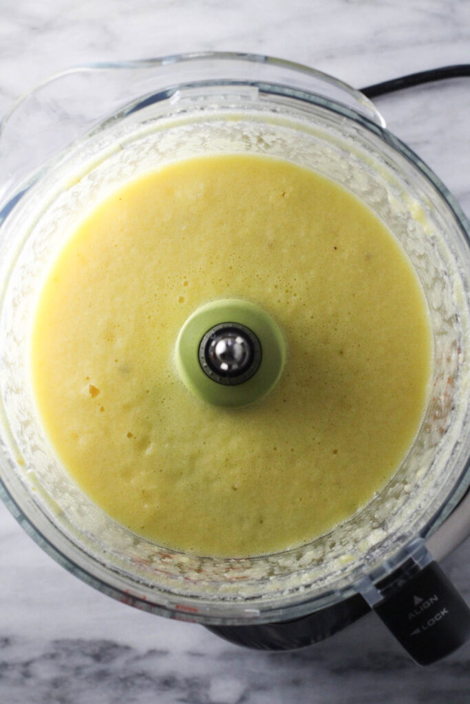 Pureed coconut in a bowl of a food processor.