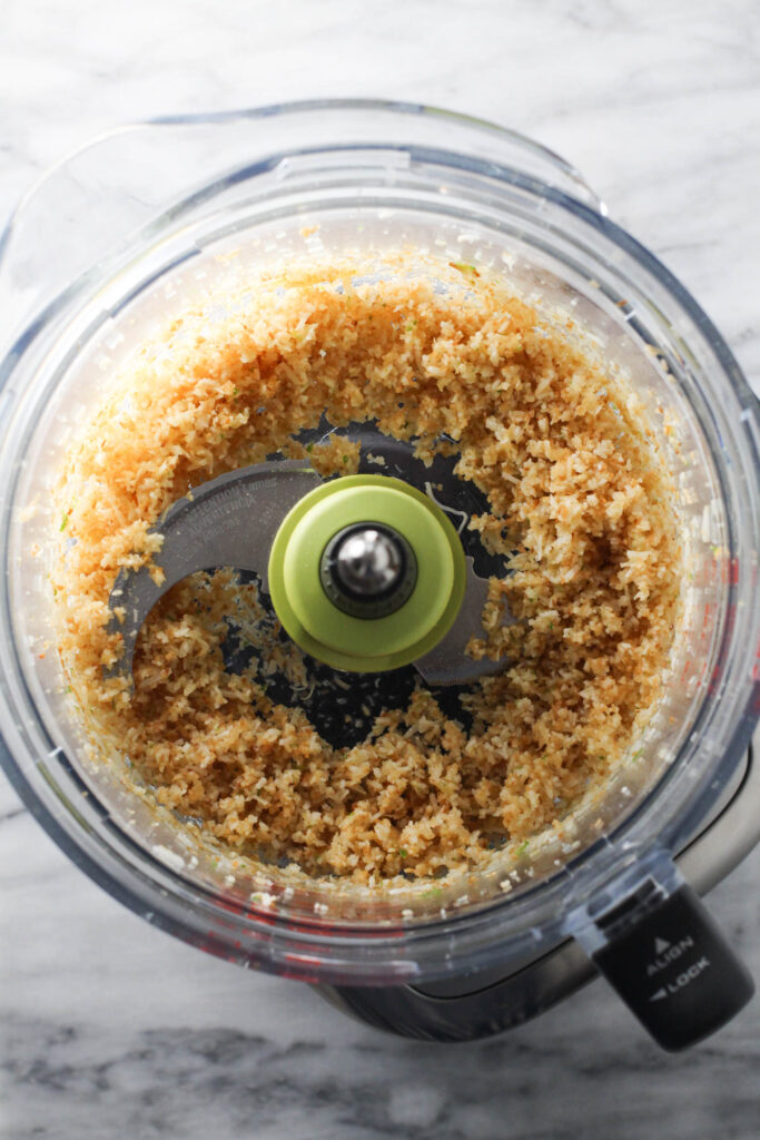 Toasted shredded coconut in a bowl of a food processor.