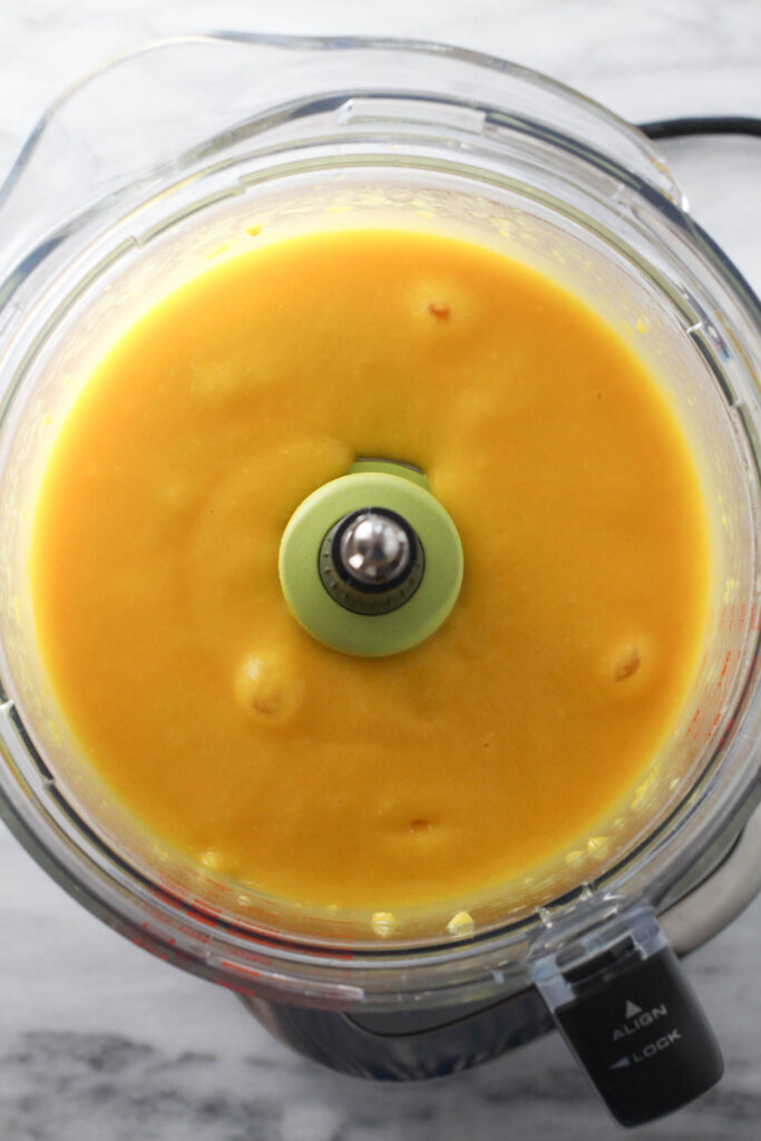 Pureed mango in bowl of a food processor.