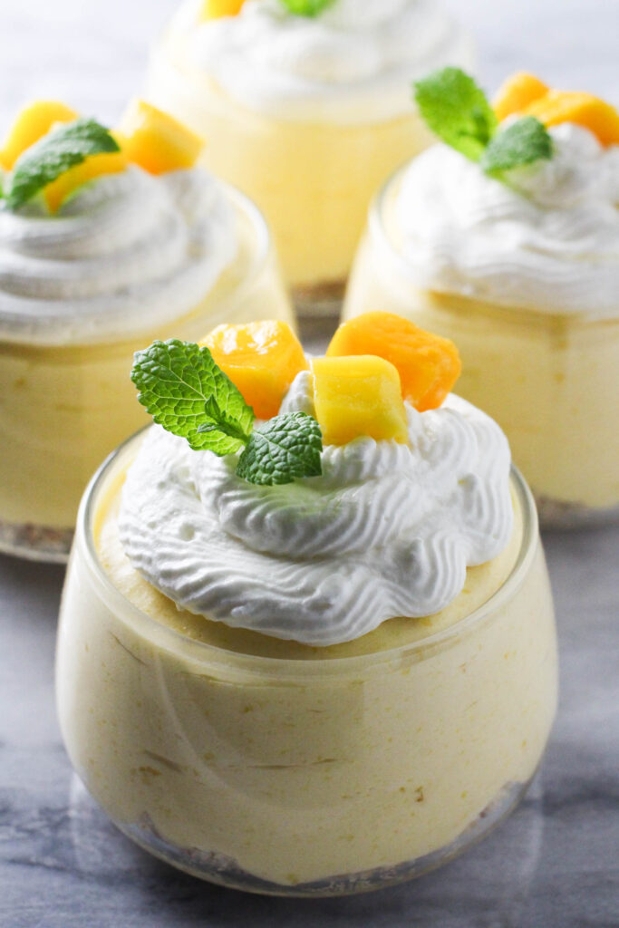 Mango mousse in a glass dessert bowl. Garnished with whipped cream, mango slices and fresh mint.