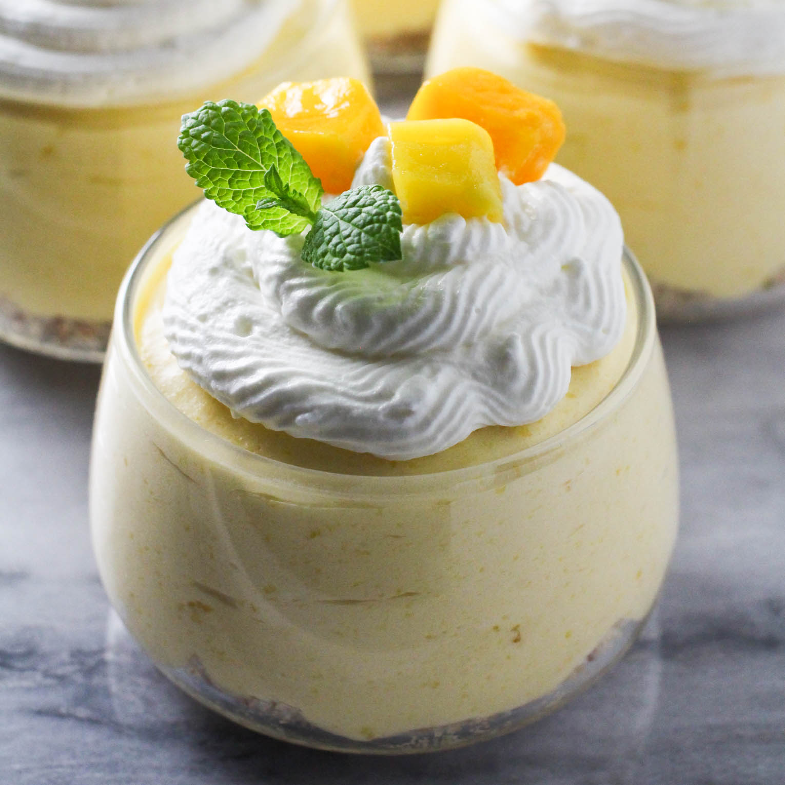 Mango mousse in a glass bowl garnished with whipped cream, mango slices and fresh mint.
