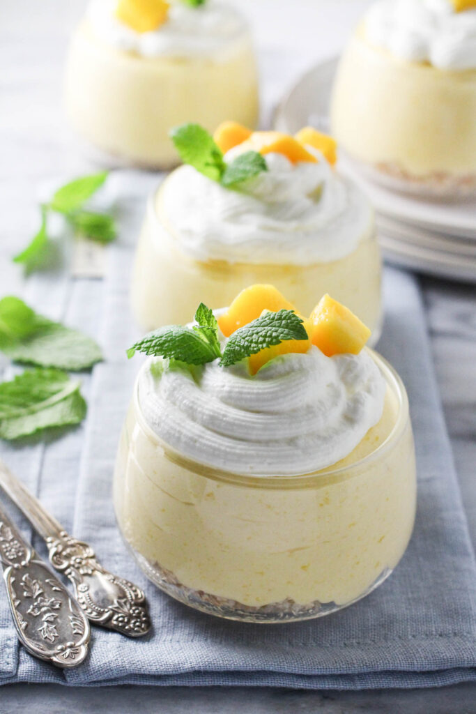 Four dessert bowls with mango mousse garnished with whipped cream, mongo slices and fresh mint.
