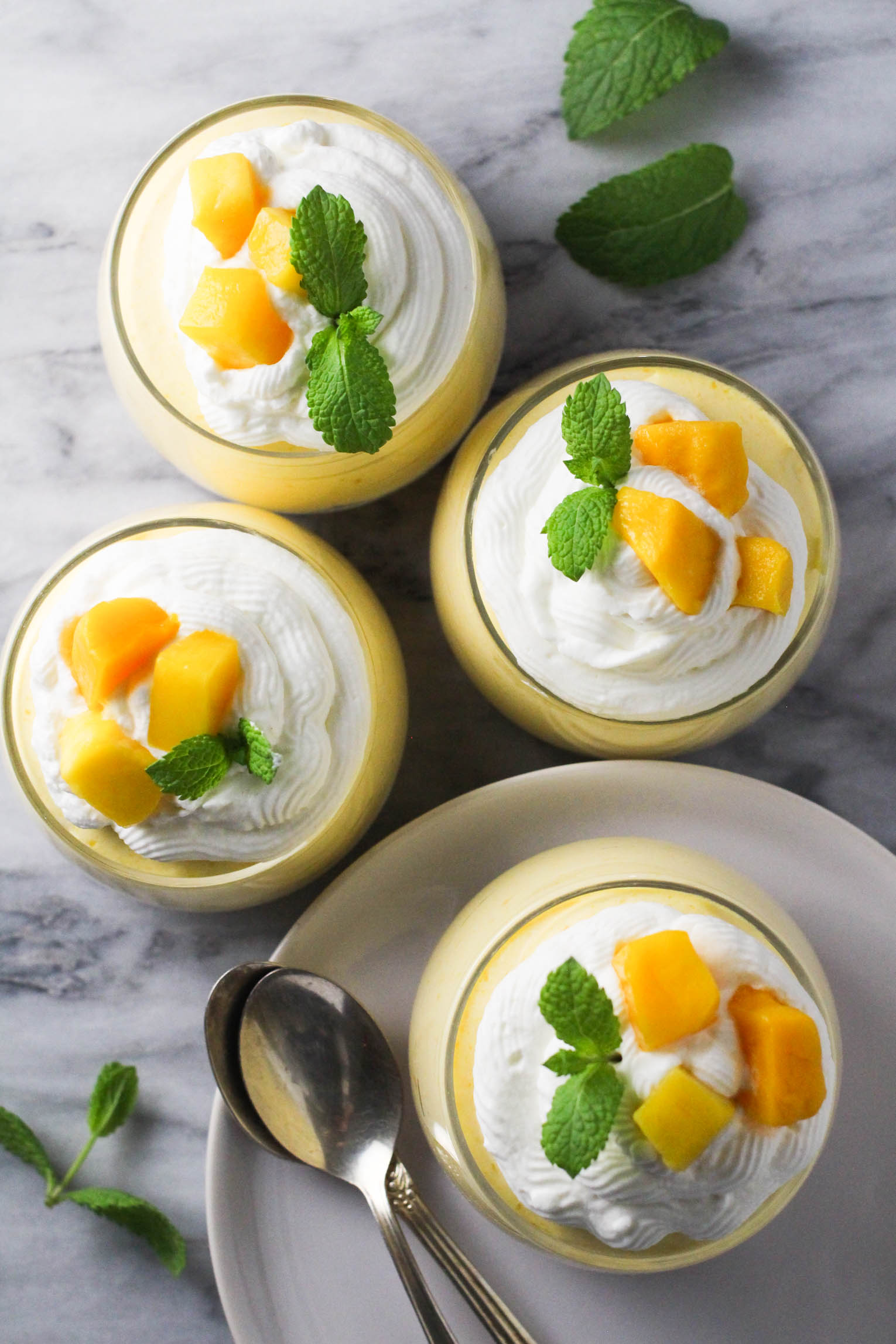 Overhead shot of four mango desserts on marble background.
