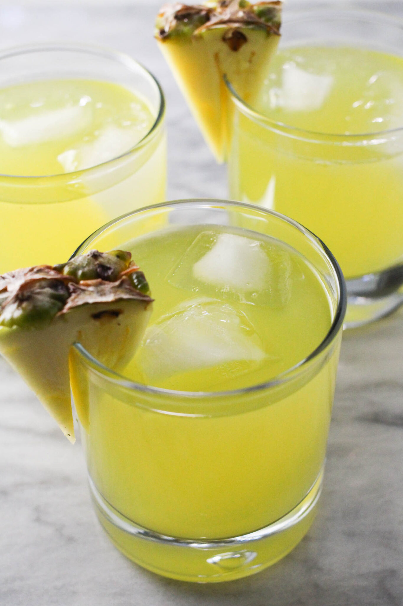 Three glasses of pineapple coconut water with ice, garnished with pineapple slices.
