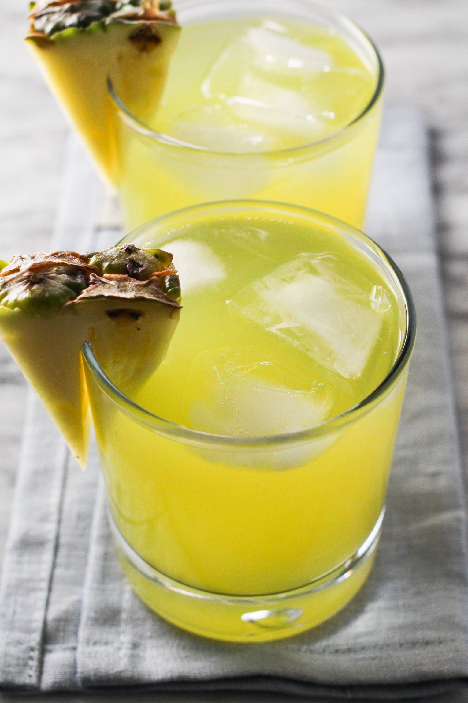 Two glasses of pineapple coconut water with ice cubes, garnished pineapple slices.