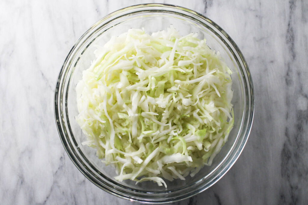 Shredded cabbage in a bowl standing on a marble background.