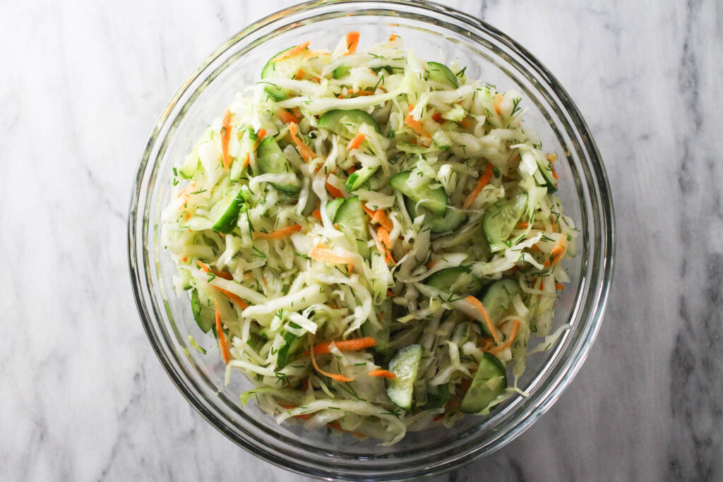 Cabbage cucumber salad in a glass bowl standing on marble background.