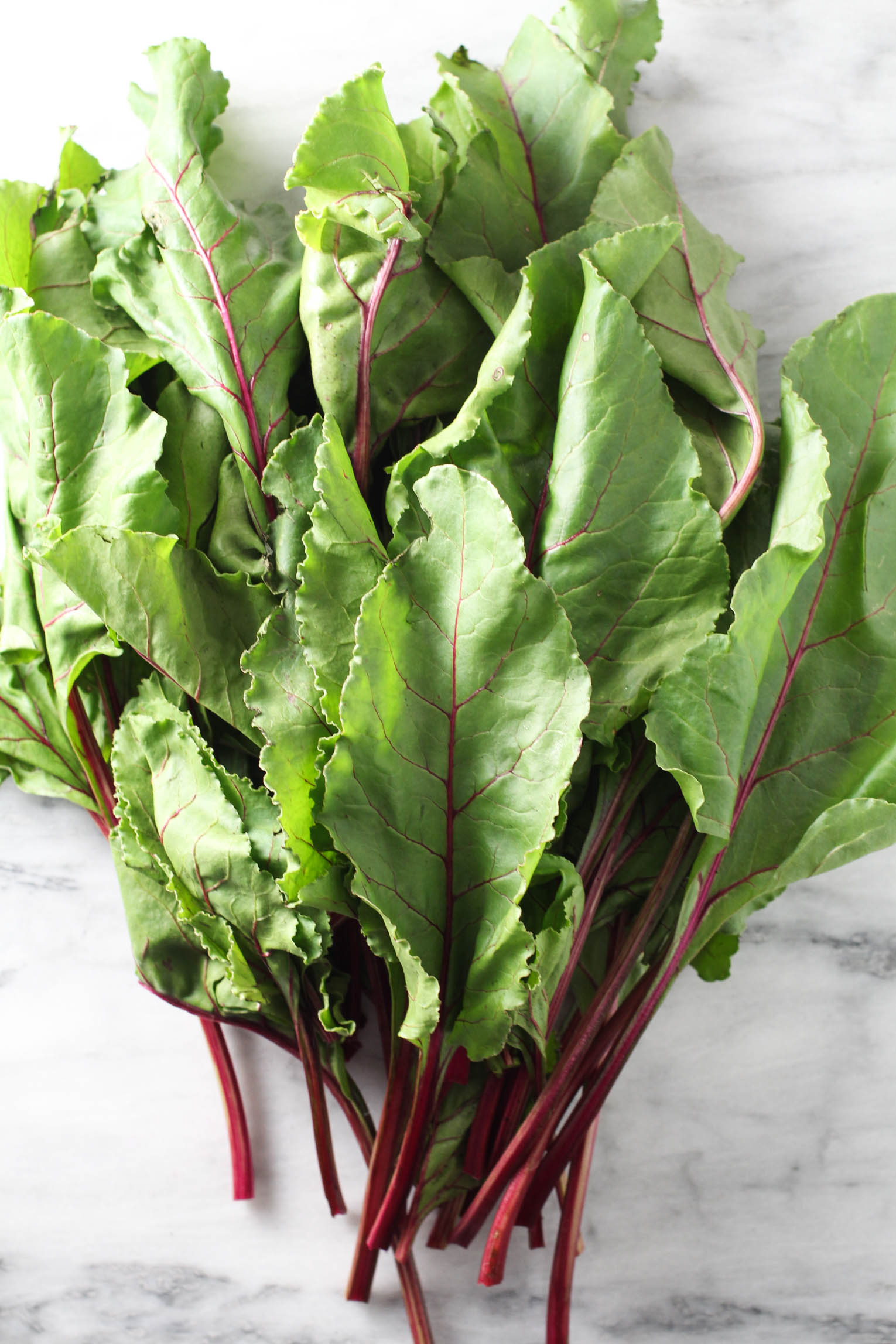 A bunch beet greens on marble background.