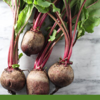 A bunch of fresh beets with greens on a marble background. Below the image, there is a text overlay saying: what to do with beet greens, recipes + tips.