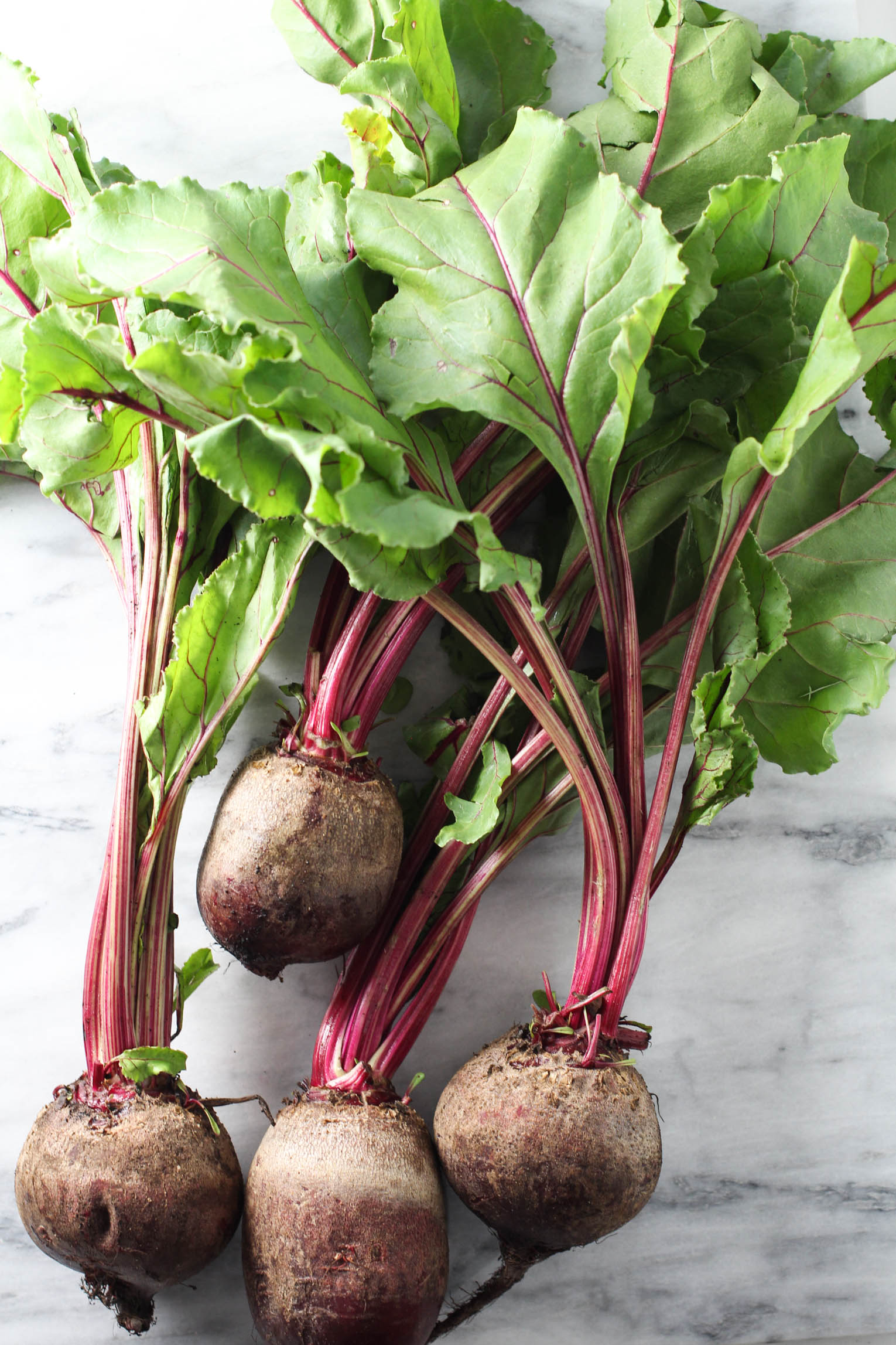 A bunch of beets with greens on marble background.