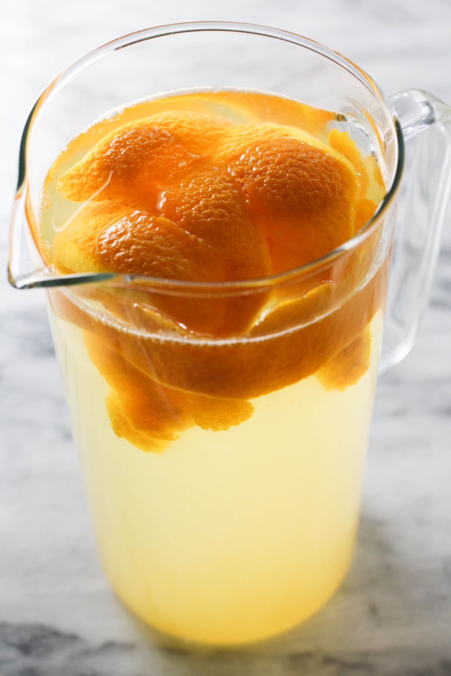 A pitecher of orange water with orange peel in it.