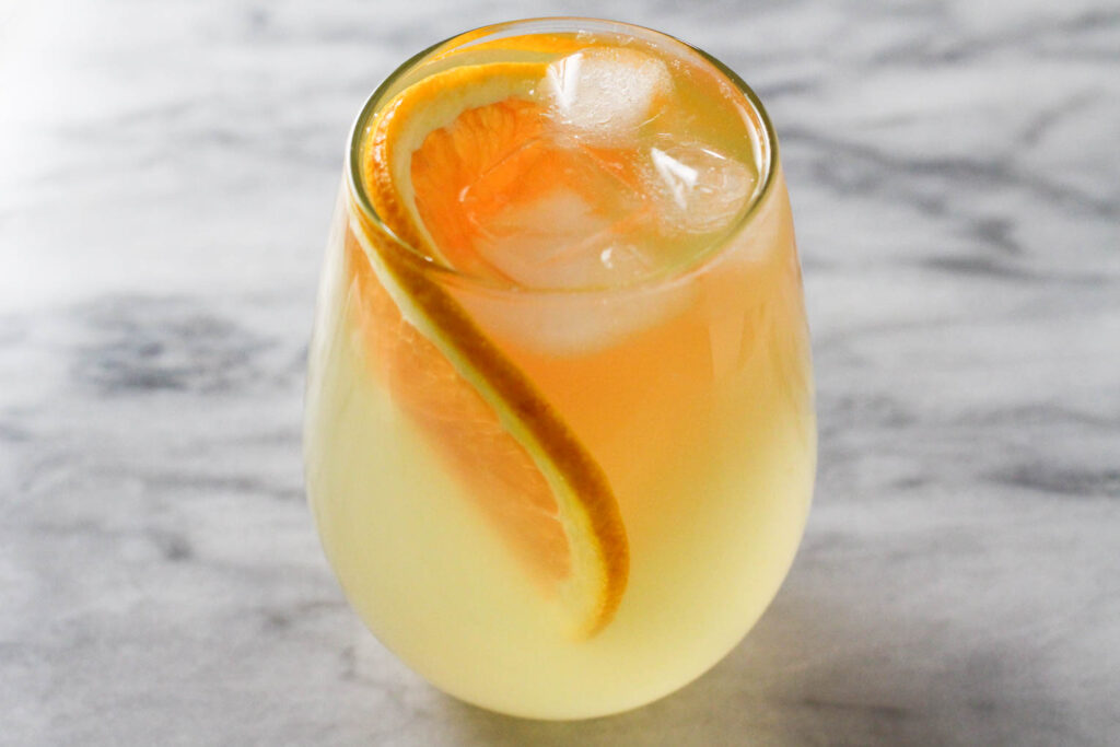 A glass on orange water with ice and a slice of orange.