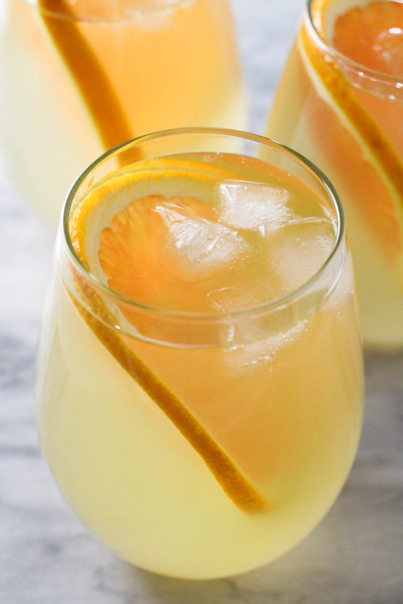 A glass of orange infused water with ice cubes and a slice of orange.