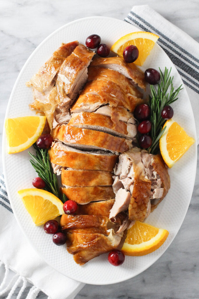 Sliced turkey on a dish, garnished with rosmary, cranberries and orange slices.