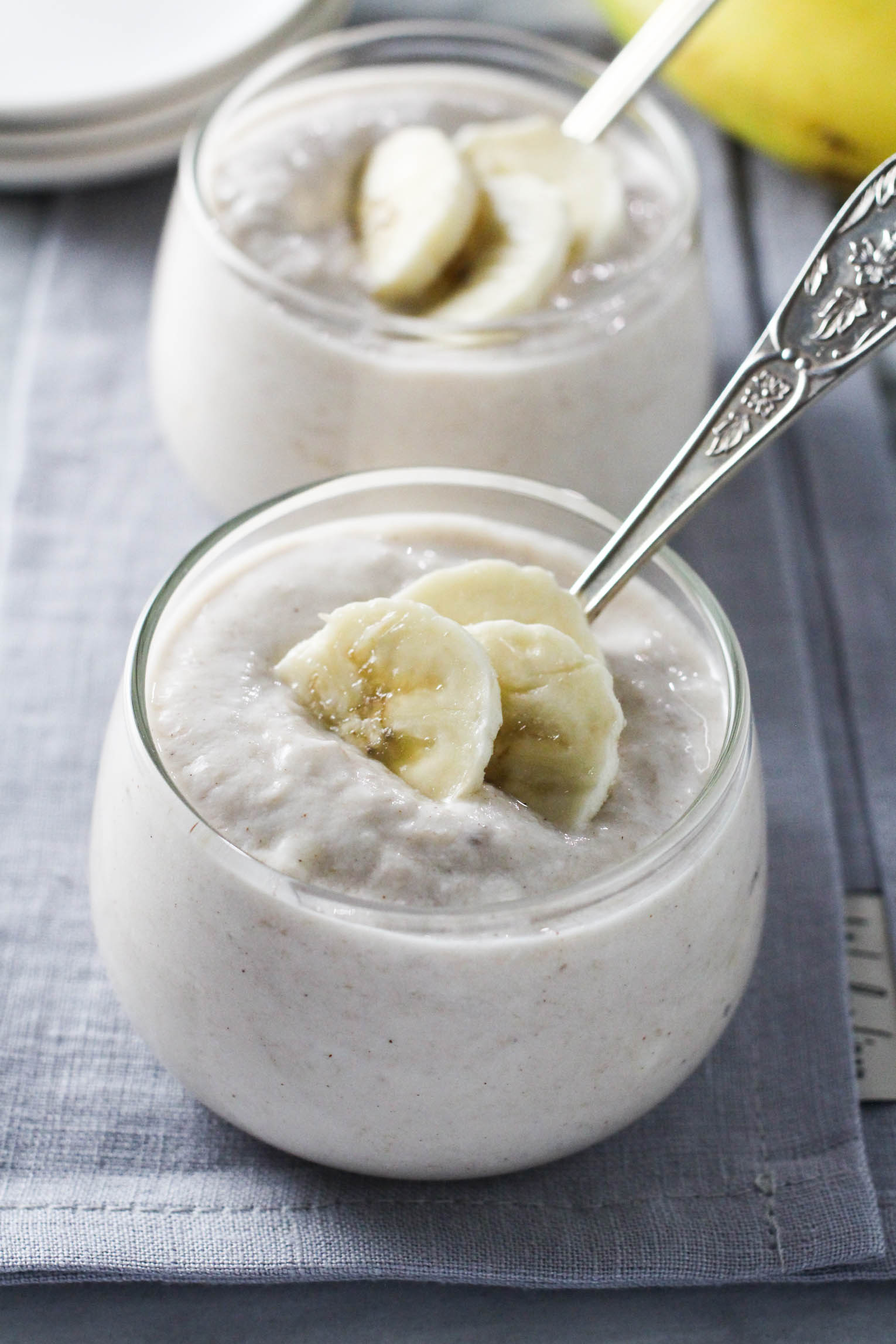 Two dessert bowls with banana yogurt with spoons in them.