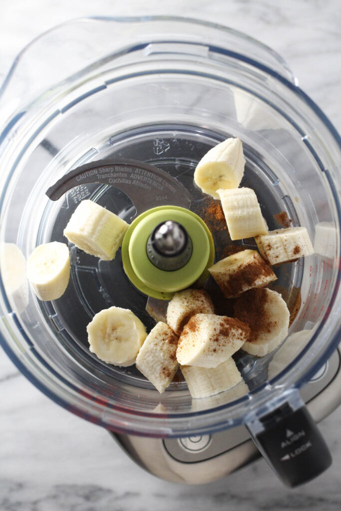 Banana slices and cinnamon in a bowl of a food processor.