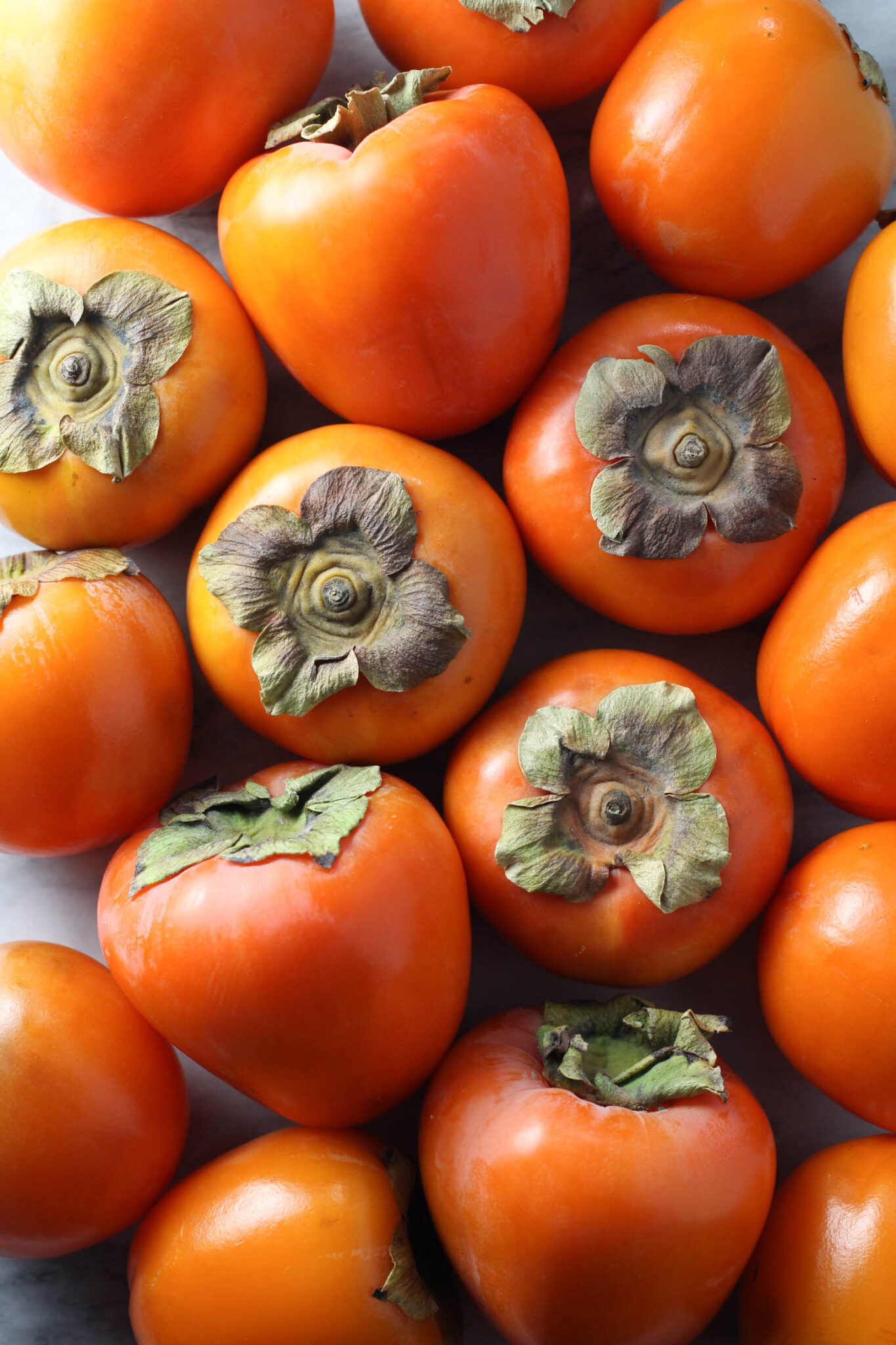 Overhead shot of persimmons displayed on marble background.