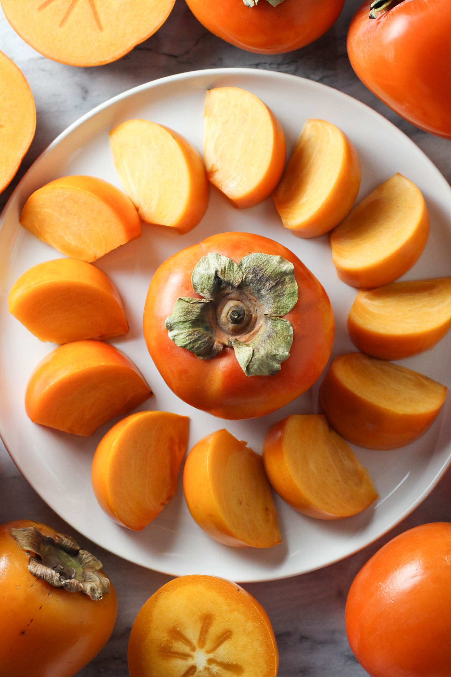 Fuyu persimmons on a plate with a whole fruit in the middle.