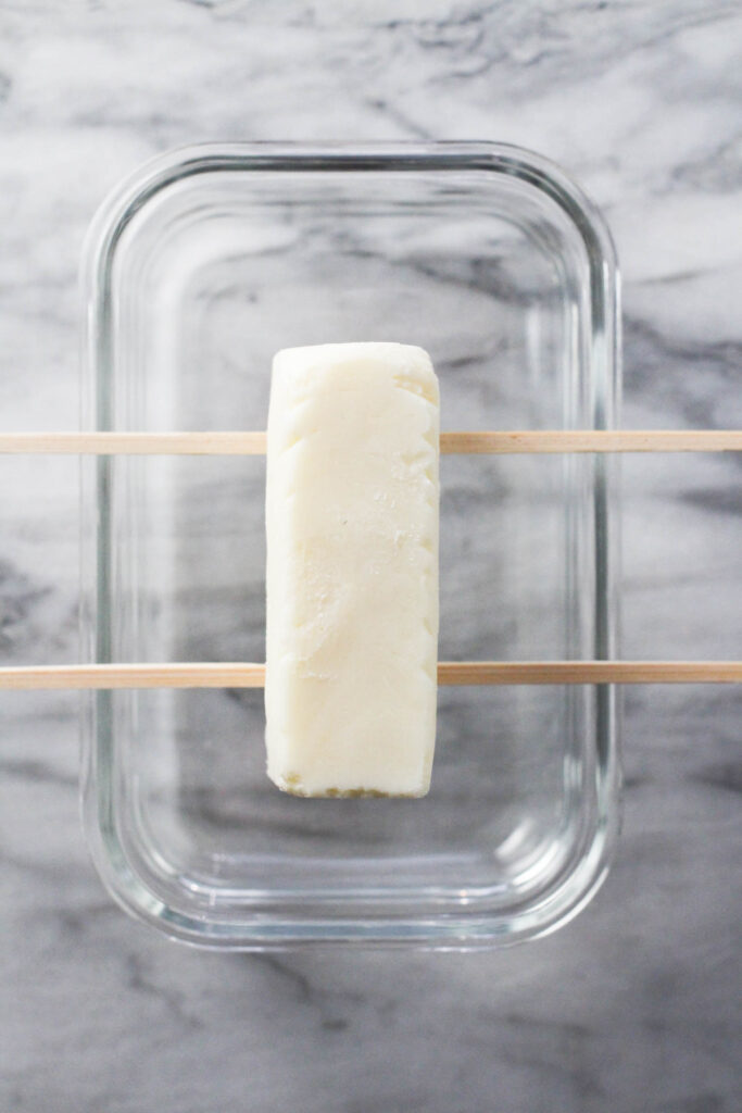 Frozen bar on top of skewers over a glass container.