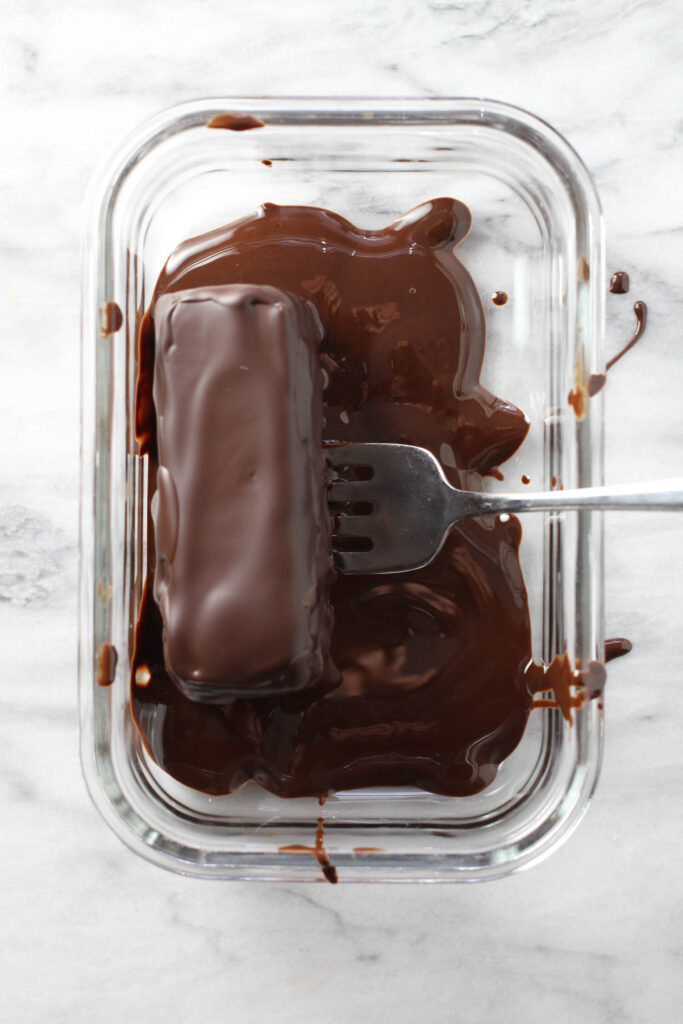 Chocolate glazed syrok on fork in the glaz container with the chocolate glaze on the bottom.