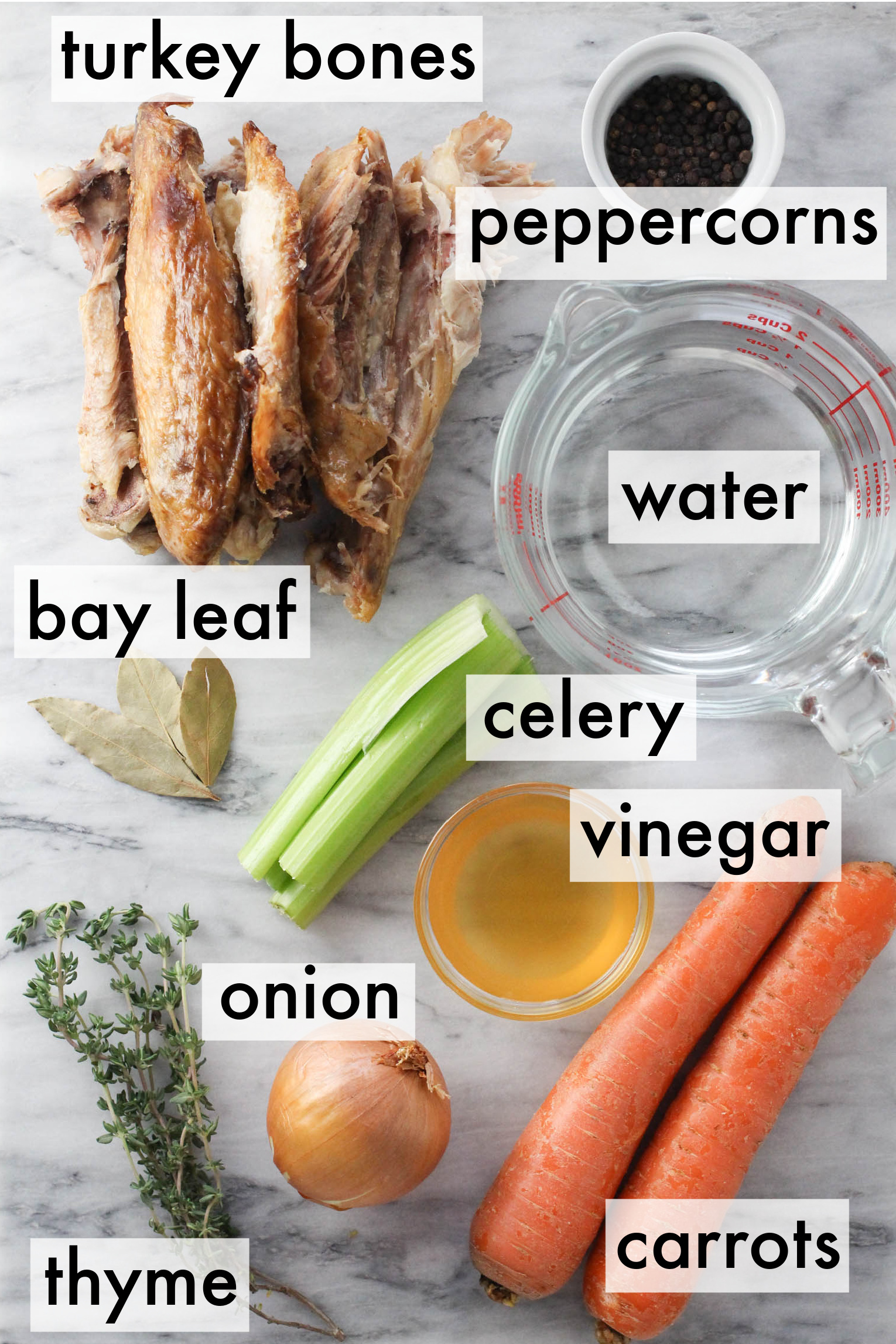 Turkey bone broth ingredients displayed on marble background. The ingredients are labeled as follows: turkey bones, peppercorns, water, bay leaf, celery, vinegar, onion, thyme, carrots.