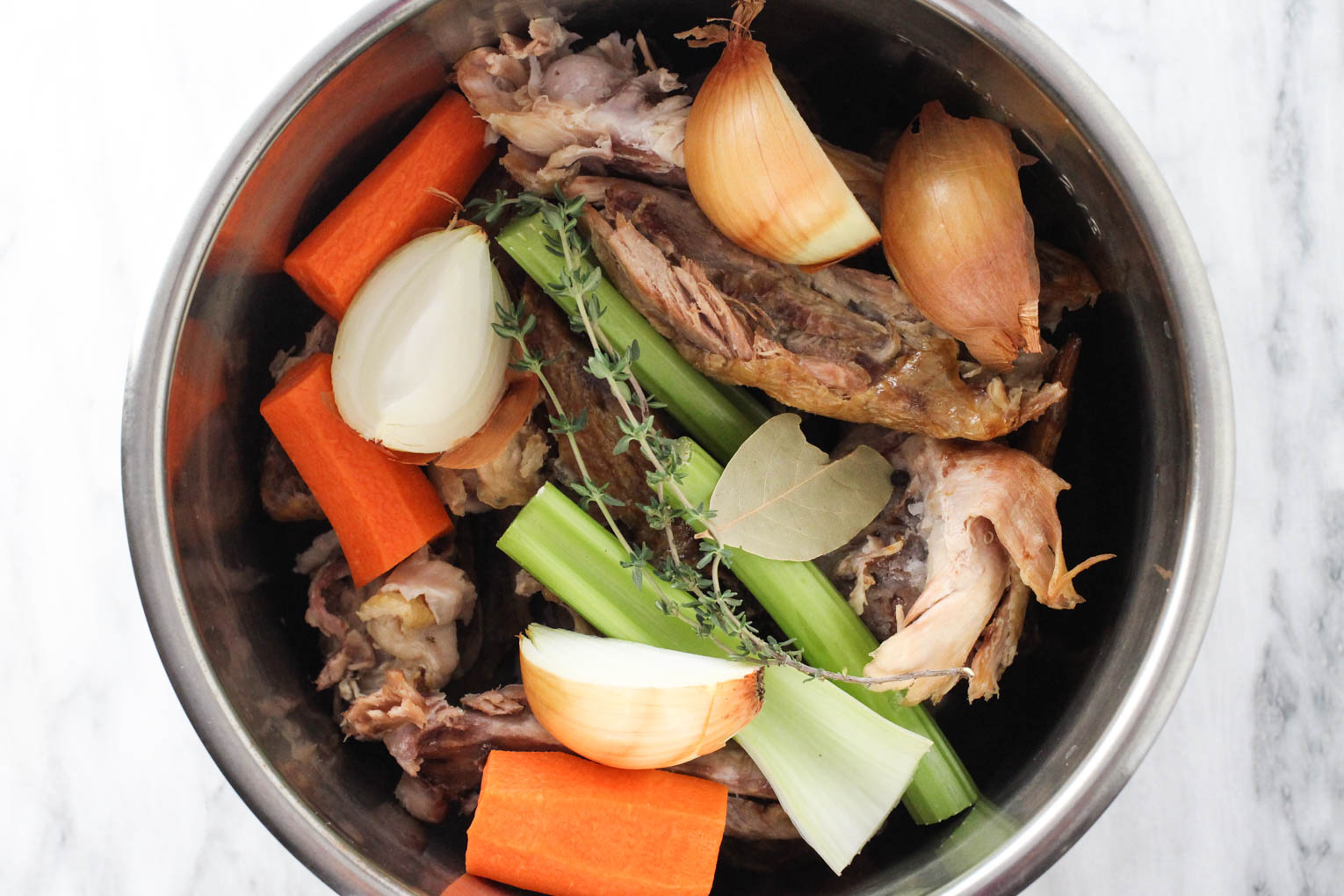 Turkey bones, vegetables and spices inside Instant Pot inner cooking pot.
