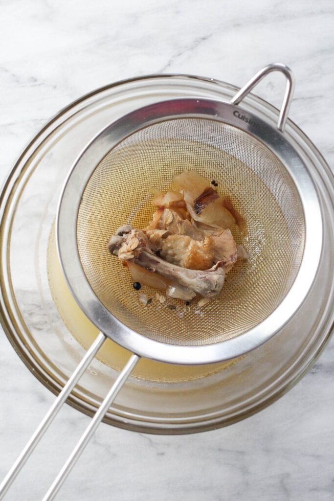 A fine mesh strained with turkey bones and other solids above a bowl with the broth.