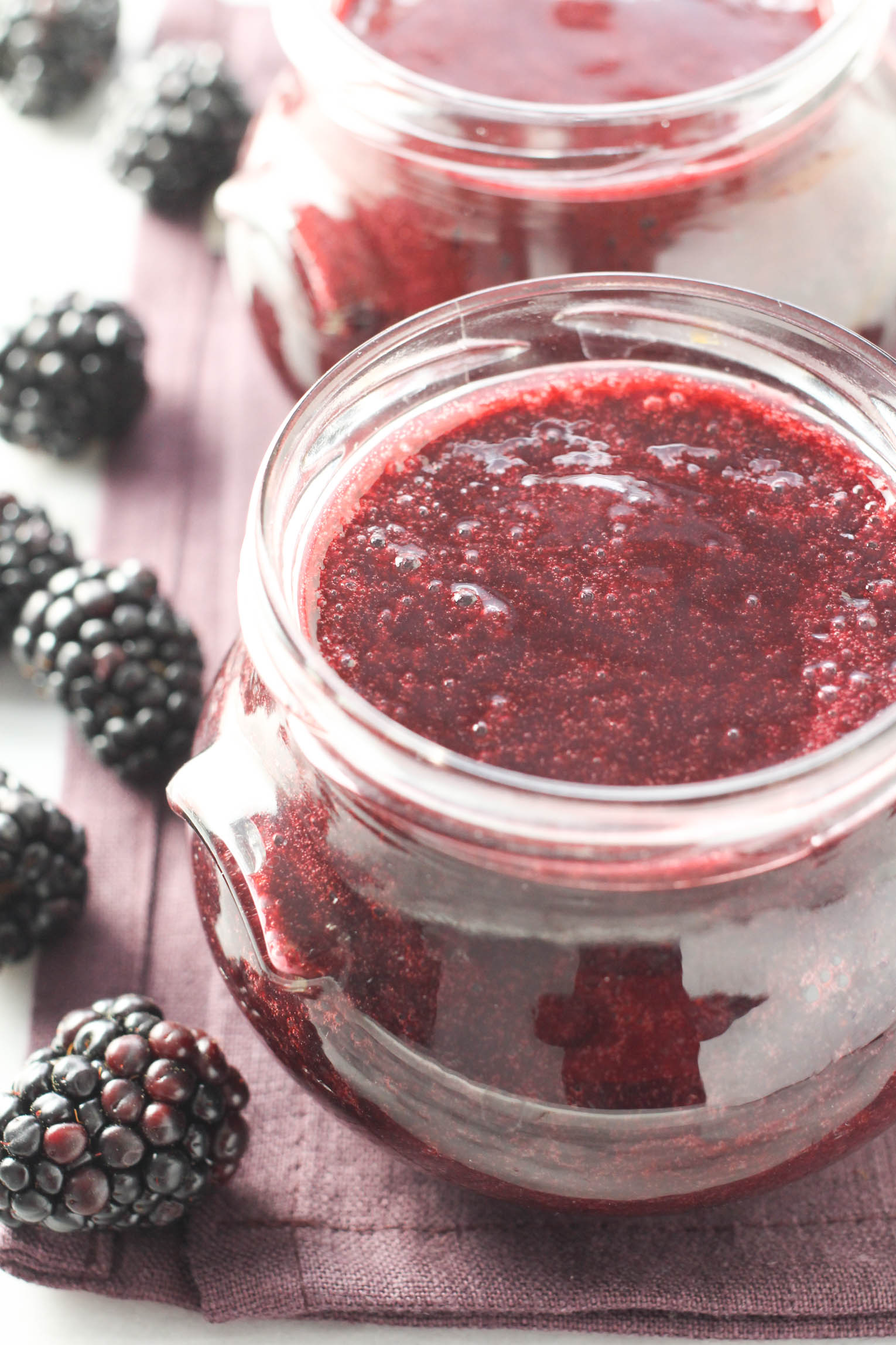 A glass jar of blackberry puree with fresh blackberries to the left.