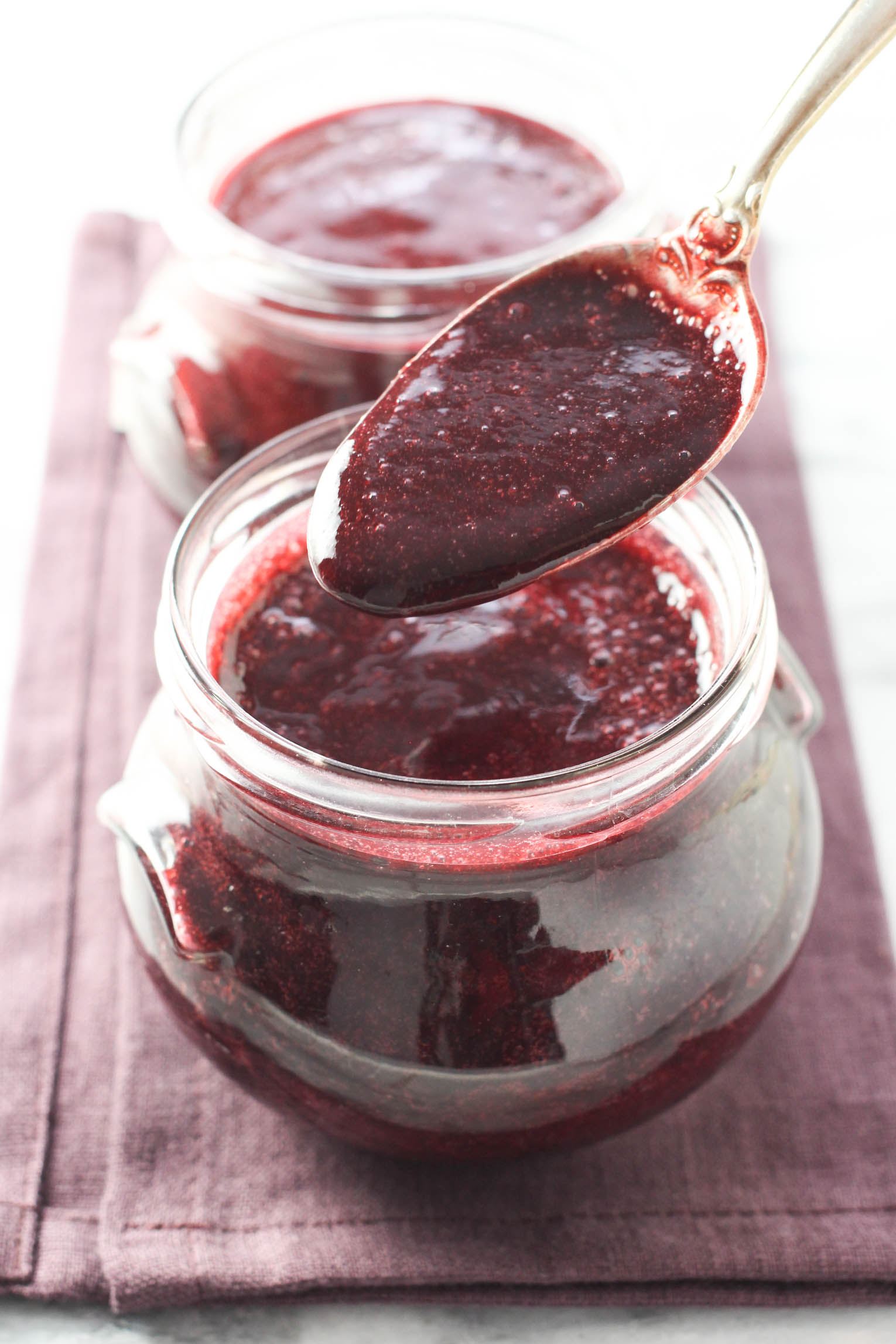 Blackberry puree being scooped out of a glass jar with a spoon.