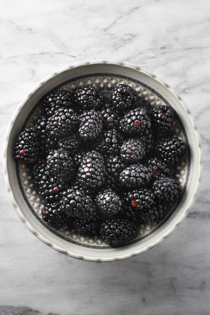 Overhead shot of fresh blackberries in a blowl standing on marble background.