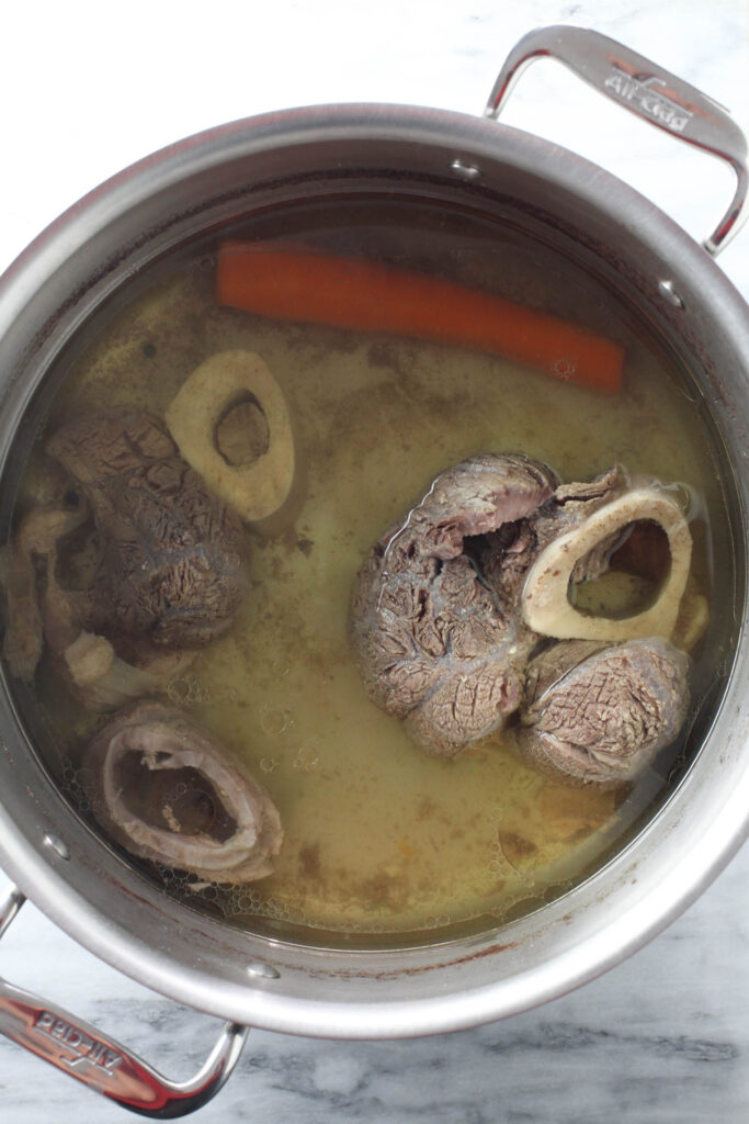 Cooked beef broth with ingredients in a soup pot.
