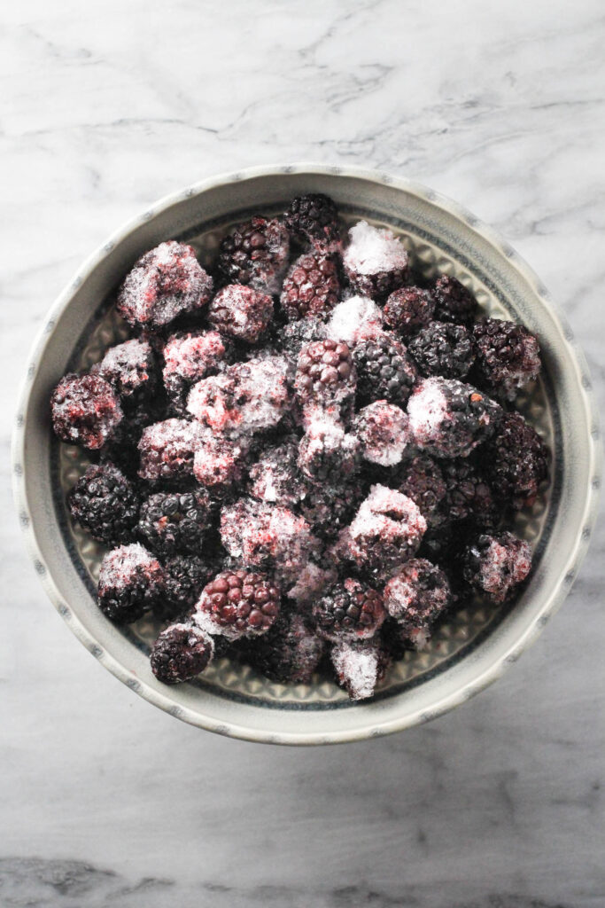 Overhead shot of frozen blackberries in a blowl standing on a marble background.