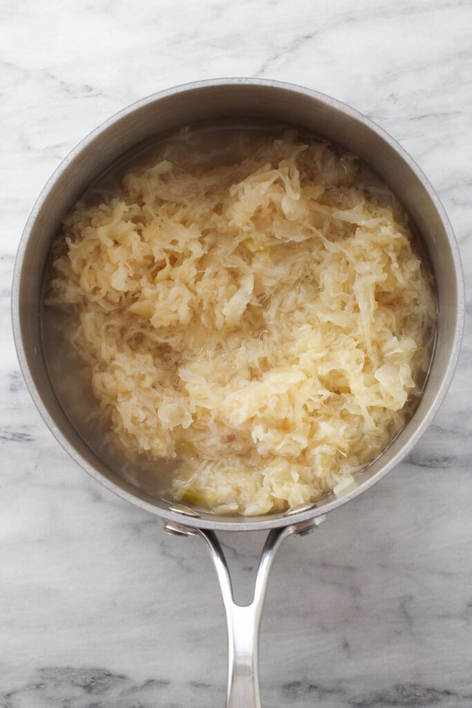 Sauerkraut in a saucepan standing on marble background.