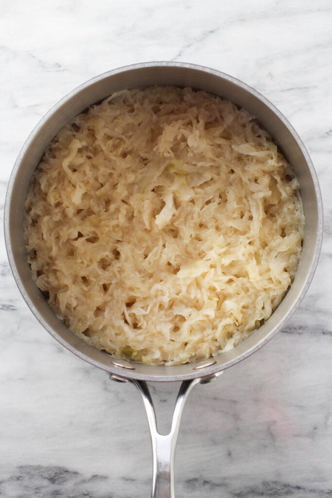 Simmered sauerkraut in a saucepan standing on marble background.