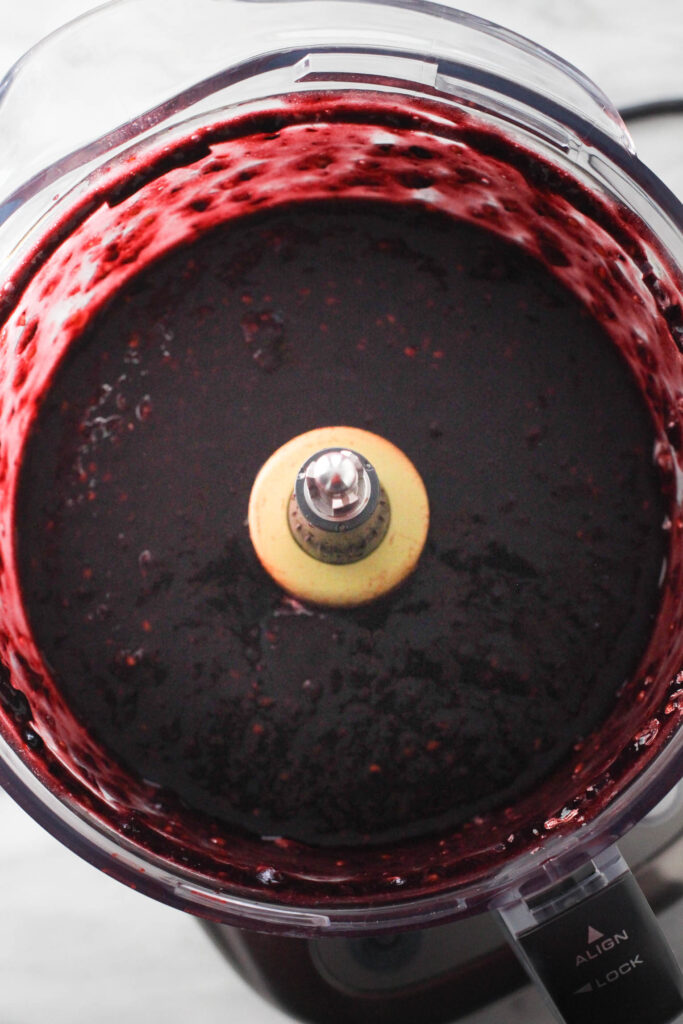 Pureed black berries in a bowl of a food processor.
