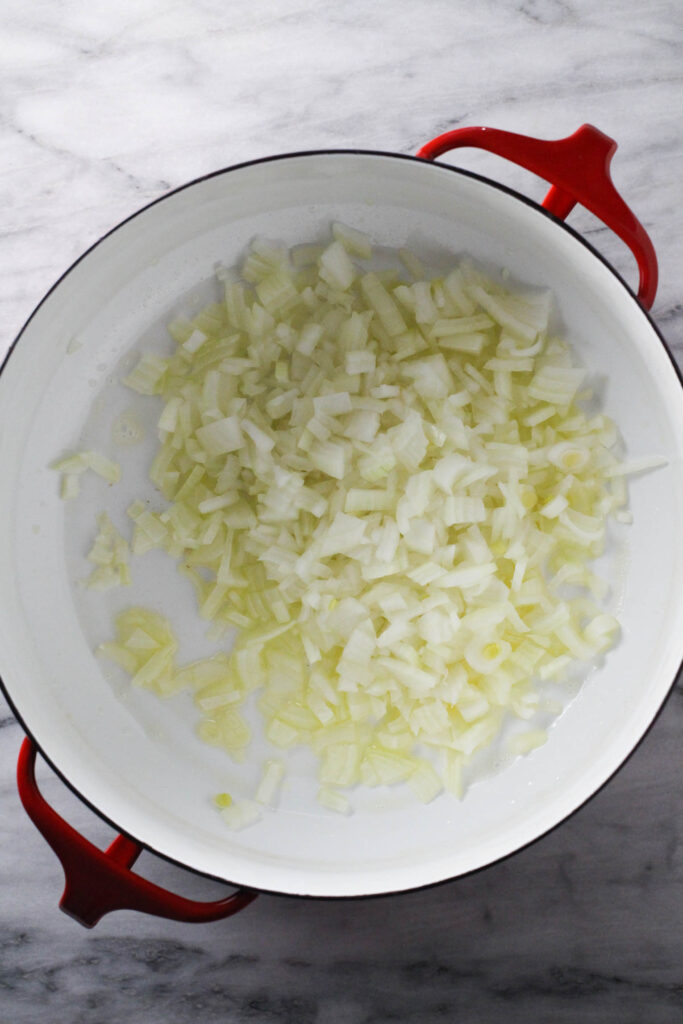 Sliced onions in a soup pot standing on marble background.