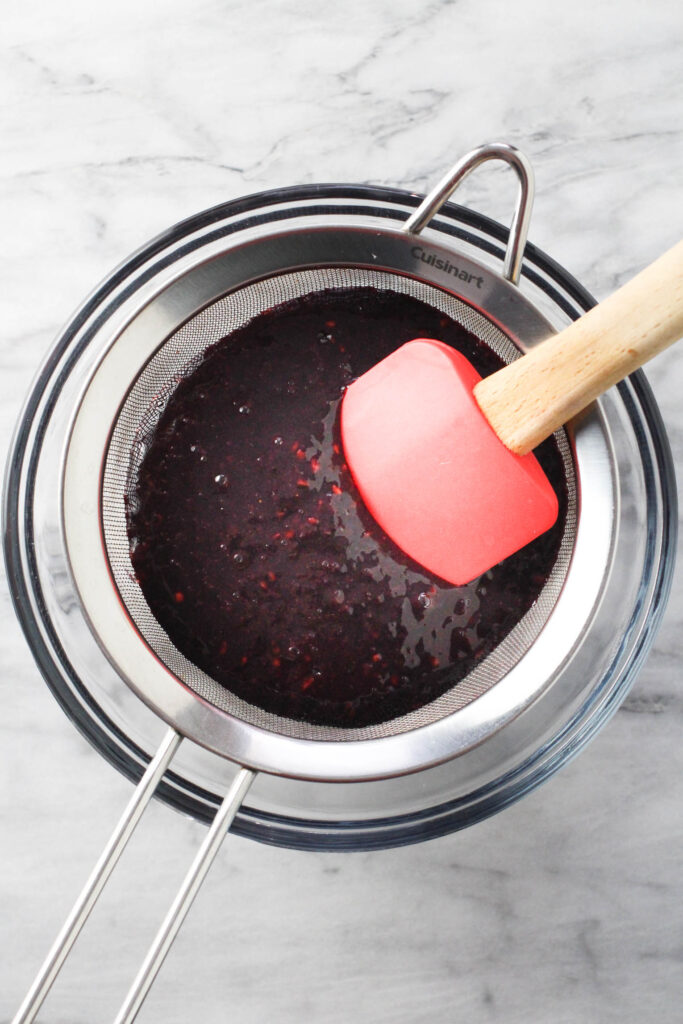 Pureed blackberries in a fine mash sieve placed over a bowl.