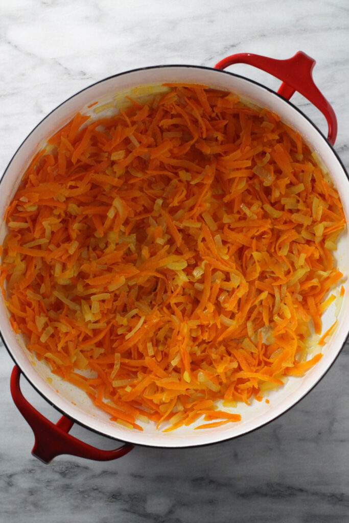 Sauteed onions and carrots in a soup pot standing on marble background.
