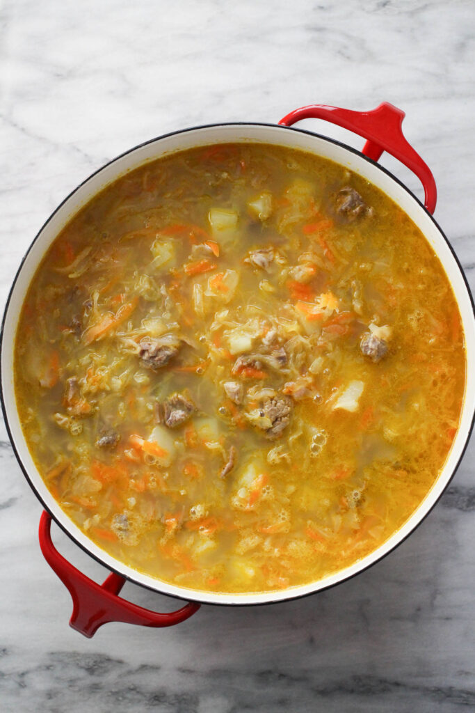 Cooked shchi in a soup pot standing on marble background.