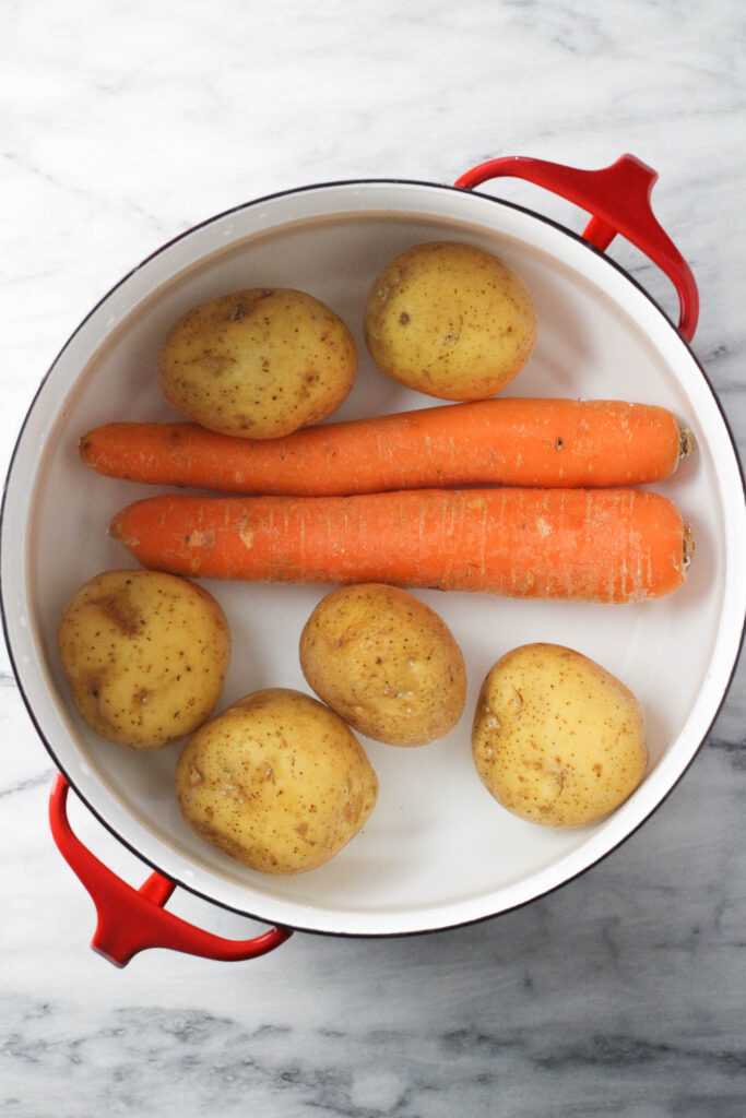 Overhead shot of potatoes and carrots in a pot of water.