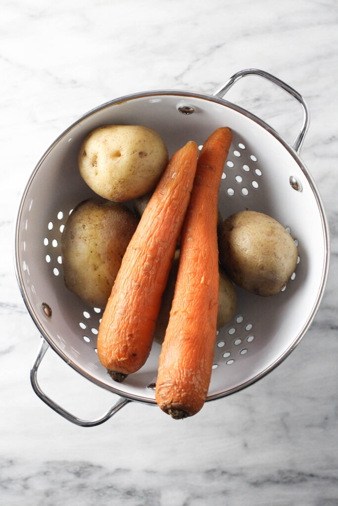 Overhead shot of cooked carrots and potatoes in a strainer.