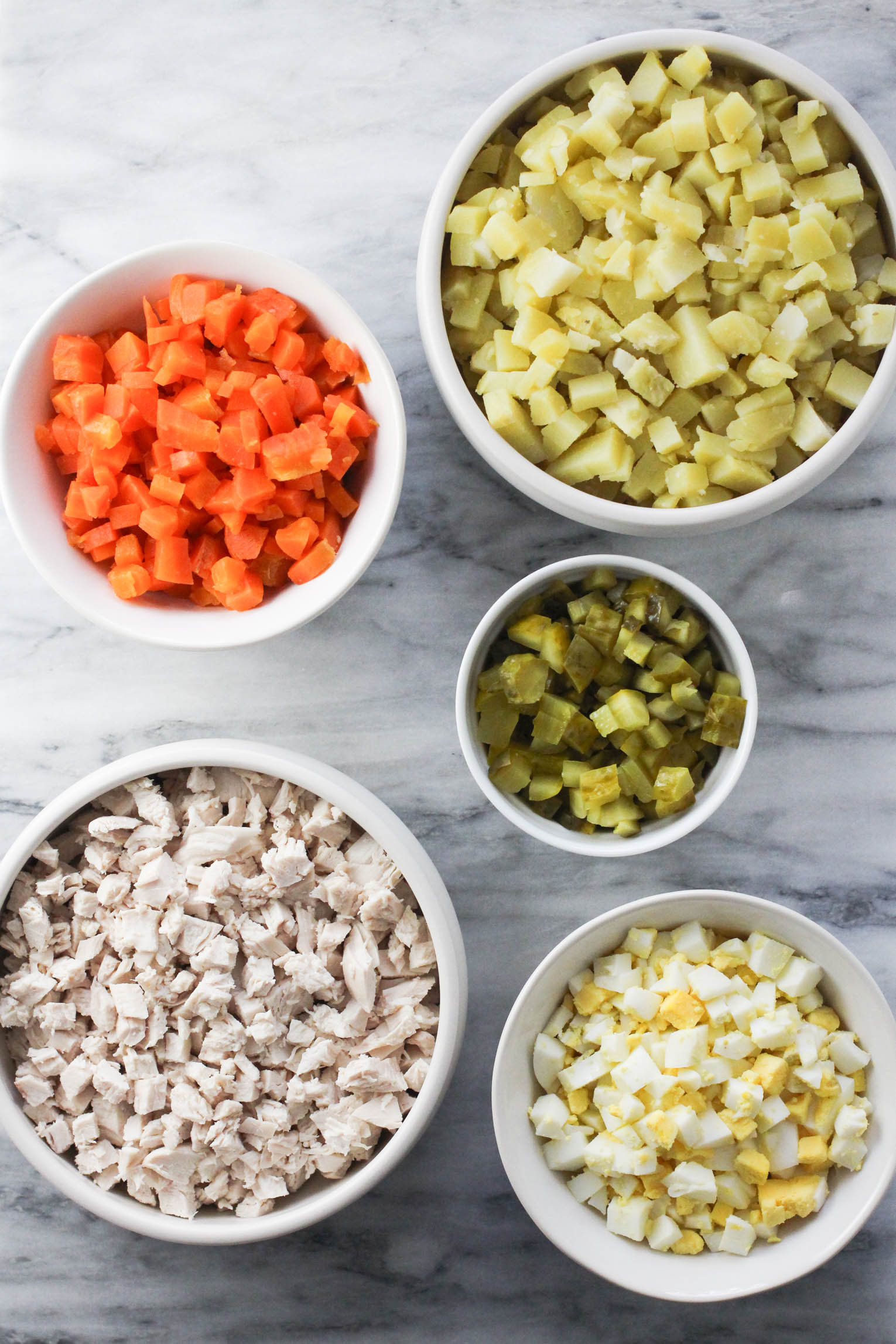 Evenly diced potatoes, carrots, pickles, meat and eggs in bowls.