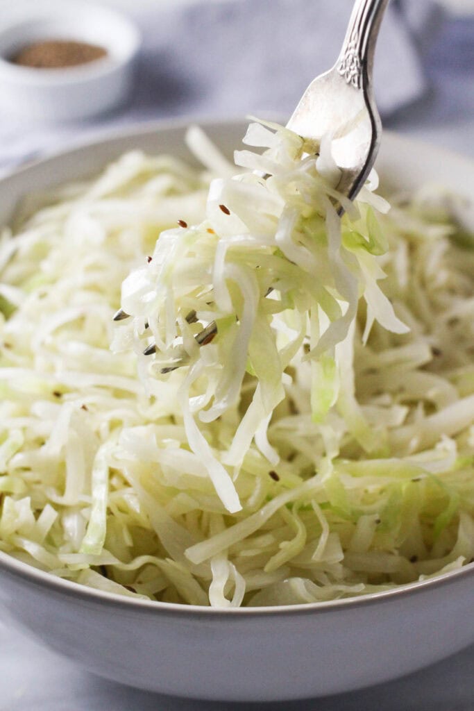 Fork holding a portion of Krautsalat with bowl of salad in background.