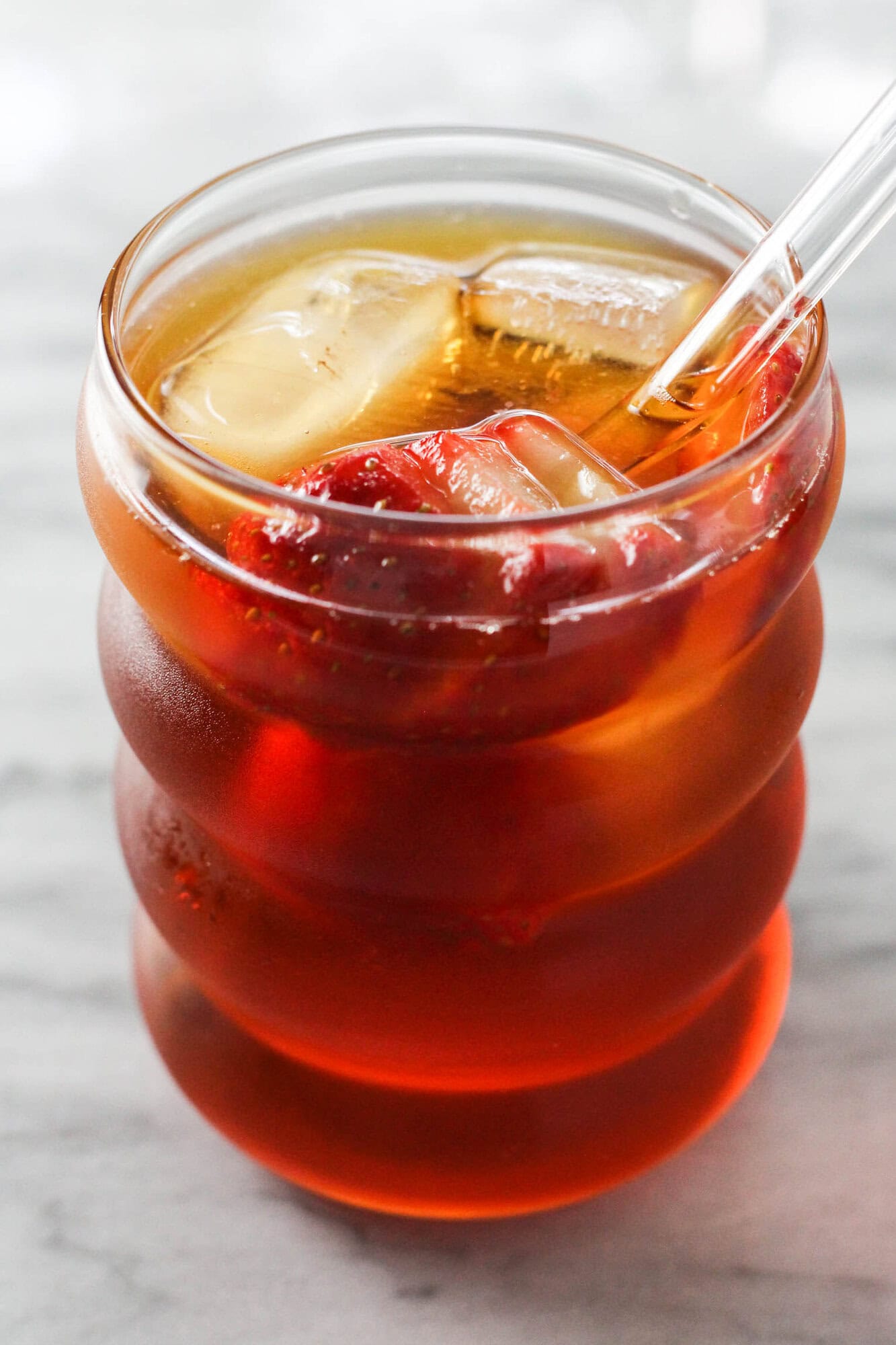 Strawberry iced rooibos tea in a glass with ice cubes and sliced strawberries, ready to serve.